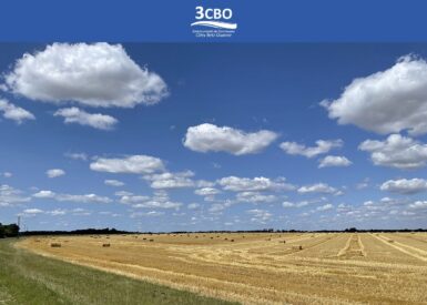 Ciel bleu avec des nuages blancs au dessus d'un champ de blé avec des ballots de pailles
